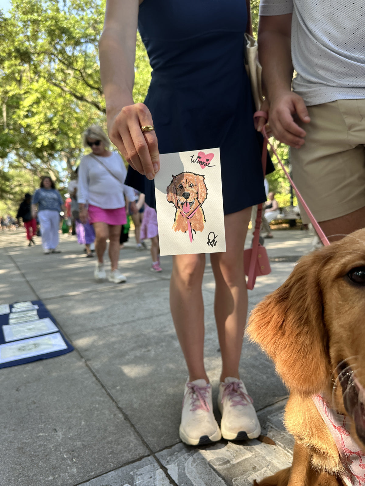 A customer holding a finished painted portrait of Winnie at the Forsyth Park Artists' Market